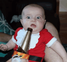 a baby in a santa costume is holding a bottle of beer