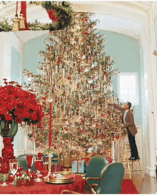 a man on a ladder decorates a christmas tree in a room