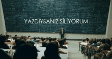 a man stands in front of a large blackboard with the words yazdiysaniz siliyorum on it