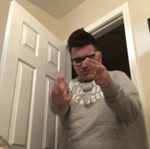 a man wearing glasses and a grey new york sweatshirt is giving the middle finger