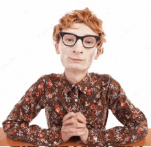 a man with glasses is sitting at a desk with his hands folded .