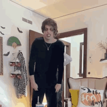 a man in a black shirt is standing in a living room next to a chair .