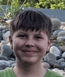 a young boy in a green shirt is smiling for the camera while standing in front of a pile of rocks .