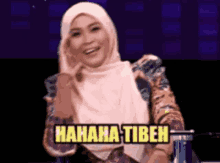 a woman in a hijab is sitting in front of a sign that says '  hahaha tibeh '