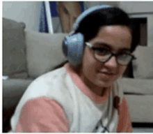 a young girl wearing headphones and glasses is sitting on a couch .