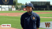 a man wearing a hat and headphones is standing on a baseball field with a sure-dry logo in the background