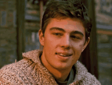 a young man wearing a tan sweater is smiling