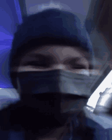 a person wearing a mask and a blue hat looks at the camera