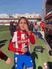 a woman in a red and white soccer uniform is standing on a field holding a can of soda .