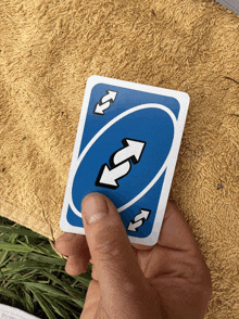 a hand is holding a blue uno card with arrows pointing in opposite directions