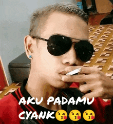 a man wearing sunglasses is smoking a cigarette with a caption that says aku padamu cyank