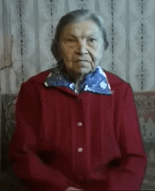 an elderly woman is wearing a red sweater and a blue scarf around her neck .