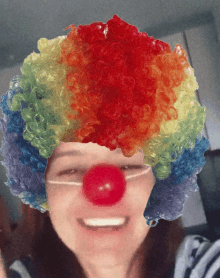 a woman wearing a clown wig and red nose smiles