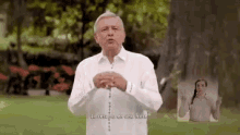 a man in a white shirt is holding a rosary in his hands while standing in front of a tree .