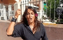 a woman in a black shirt is standing in front of a fence and holding a bottle in her hand .