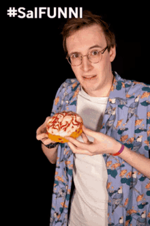 a man in a blue shirt holds a donut with a star on it in front of a sign that says #salfunni