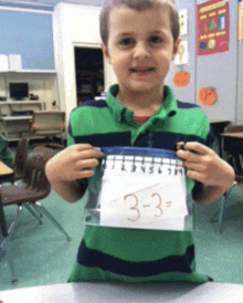 a young boy in a green and black striped shirt is holding up a piece of paper with the number three on it