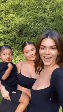 three women are posing for a picture and one of them is holding a baby who is eating a lollipop