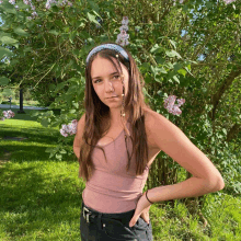 a girl wearing a headband stands in front of a tree