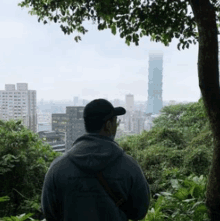 a man wearing a hat and a hoodie looking at a city skyline