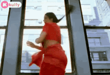 a woman in a red sari is dancing in front of a window .