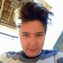 a young man wearing a striped sweater is taking a selfie with his hair in a messy bun .