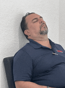 a man wearing a blue shirt with a red logo on it is sleeping on a chair