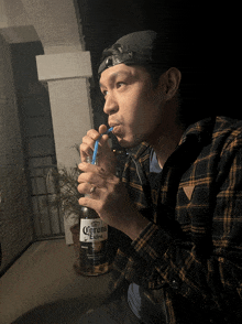 a man in a plaid shirt drinking from a bottle of corona extra