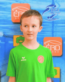 a young boy wearing a green erima t-shirt stands in front of a sign that says erd arena