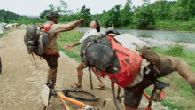 a man with a large red bag on his back is standing next to a man on a bicycle ..