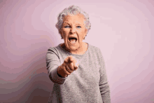 an elderly woman is screaming and pointing at the camera with her mouth open .