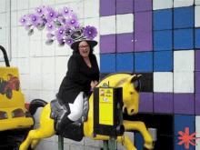 a woman wearing a purple hat is riding a yellow horse in front of a sign that says pet play