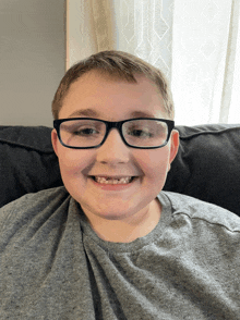 a young boy wearing glasses and a grey shirt is smiling