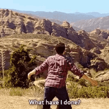 a man in a plaid shirt is standing in front of a mountain and asking what have i done ?