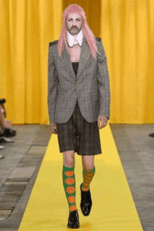 a man with pink hair and green polka dot socks walks down a runway .