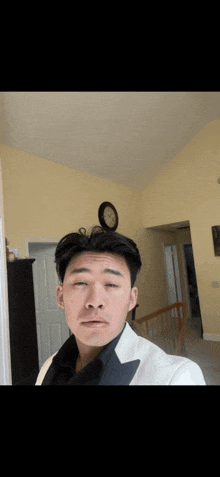 a man in a tuxedo takes a selfie with a clock on the wall behind him