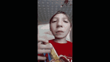 a young boy in a red shirt is eating a banana and making a funny face