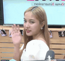 a woman in a white shirt is waving her hand in front of a tv screen that says ' thailand ' on it