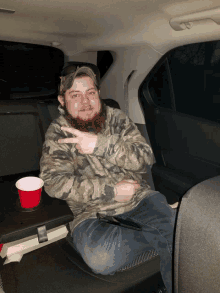 a man with a beard is sitting in the back seat of a car giving the peace sign