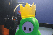 a green stuffed animal with a yellow crown on its head