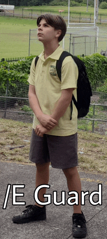 a boy with a backpack stands in front of a field with the words / e guard written below him