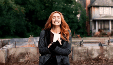 a woman with red hair is standing in front of a house holding a piece of paper in her hand .