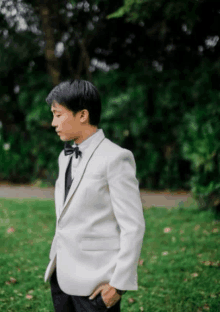 a man in a white suit and black bow tie is standing in the grass .