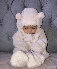 a baby in a teddy bear costume is sitting on a couch