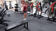 a woman stands on a bench in a gym holding a barbell in front of a sign that says ' physique '