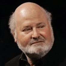 a bald man with a beard and mustache is wearing a black shirt and looking at the camera .