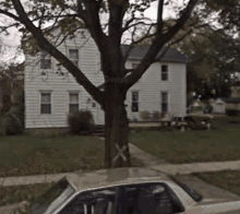 a white car is parked in front of a white house with a cross painted on the tree