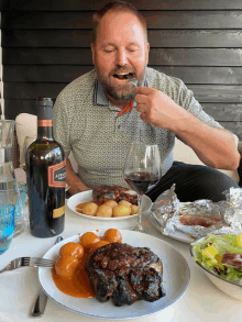 a man is sitting at a table with plates of food and a bottle of appaso wine