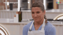 a woman wearing a blue shirt and white apron is sitting in a kitchen with the words masterchef argentina on the screen behind her