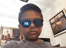 a young boy wearing sunglasses takes a selfie in front of a painting